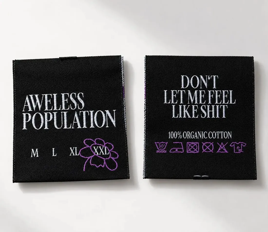 Dva všité štítky Aweless Population: velikostní s fialovou kytičkou kolem XXL a štítek s nápisem Don't let me feel like shit